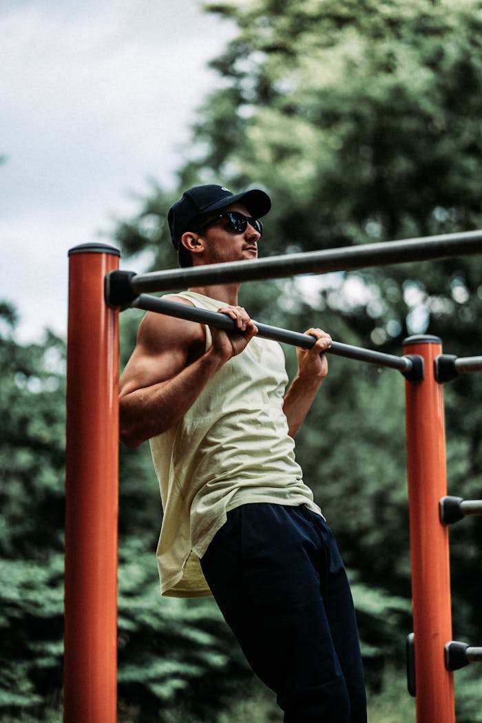 Home Man in white tank top exercising outdoors on metal bars.