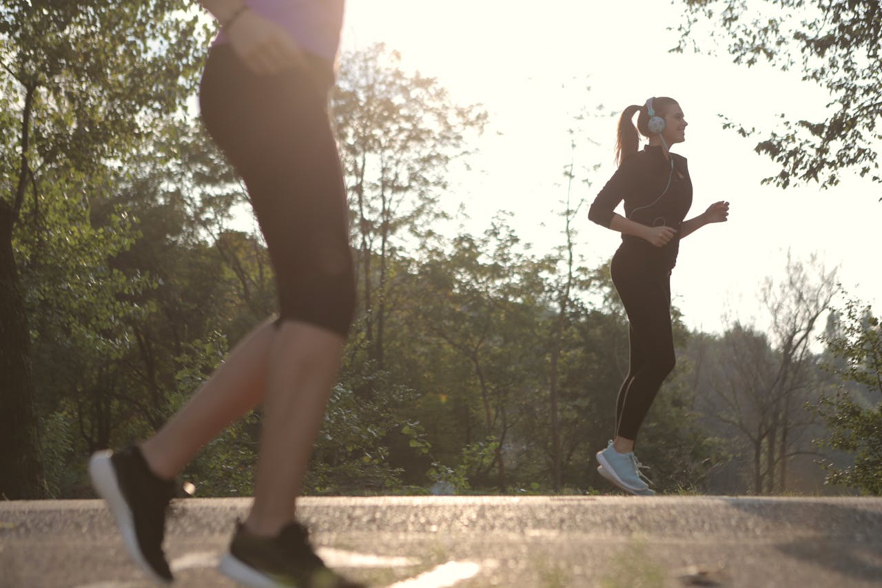 Home Two women jogging in a sunny park setting, enjoying a healthy morning exercise.