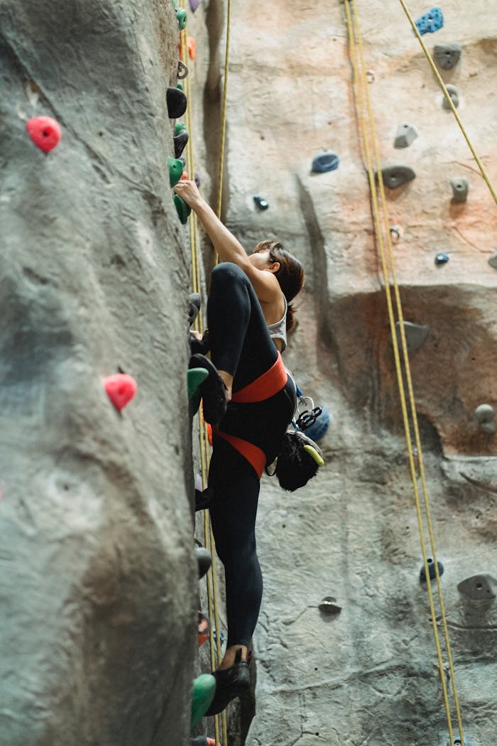 Female rock climber scaling an indoor climbing wall, demonstrating strength and agility.
